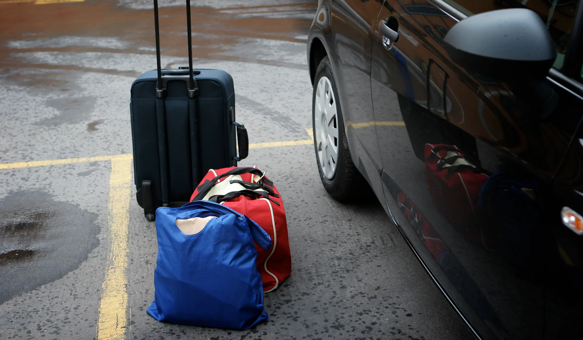 A traveller's luggage being loaded into a car at the airport curb
